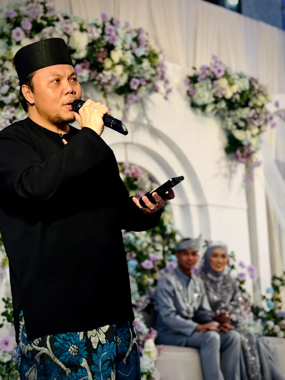 Agendas Brunei emcee mid-announcement, microphone in one hand and the run-sheet on his phone in the other